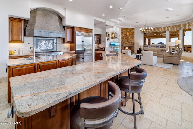 kitchen featuring custom exhaust hood, a large island with sink, a breakfast bar area, light stone countertops, and stainless steel appliances