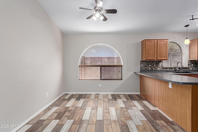 kitchen with a ceiling fan, wood finished floors, a sink, dark countertops, and backsplash