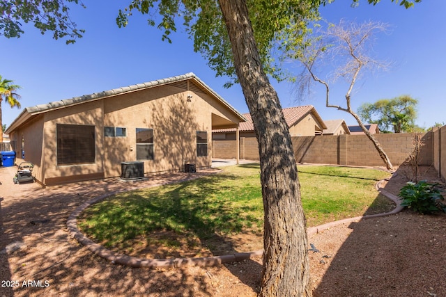 back of property with central AC unit, a fenced backyard, stucco siding, a tiled roof, and a lawn