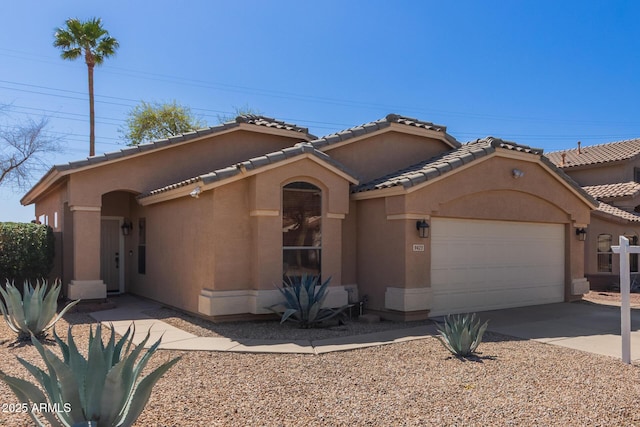 mediterranean / spanish house featuring a tile roof, stucco siding, an attached garage, and concrete driveway