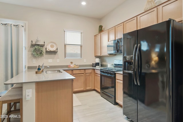 kitchen with a breakfast bar area, a peninsula, light brown cabinetry, black appliances, and a sink