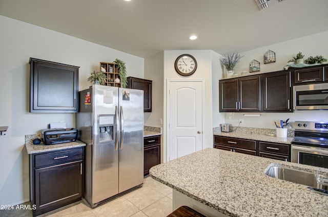 kitchen featuring light stone countertops, dark brown cabinets, stainless steel appliances, sink, and light tile patterned floors