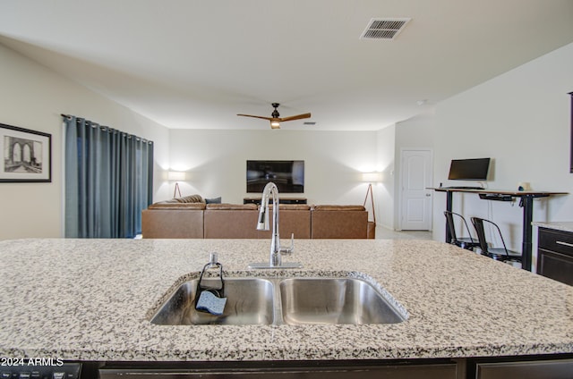 kitchen featuring a center island with sink, light stone counters, ceiling fan, and sink