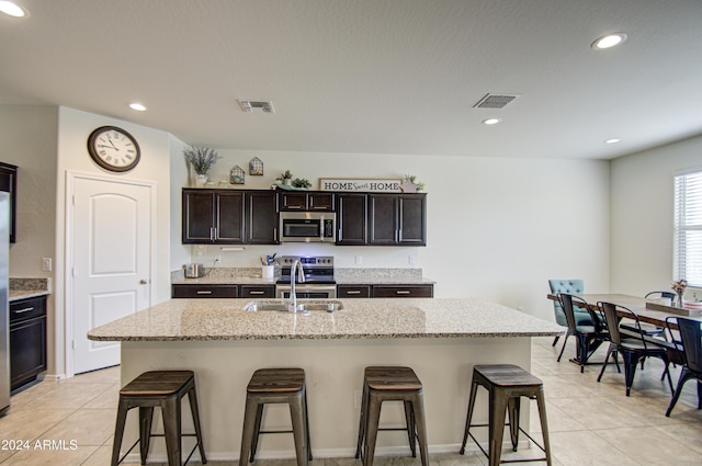 kitchen featuring light stone countertops, a breakfast bar, stainless steel appliances, a kitchen island with sink, and sink