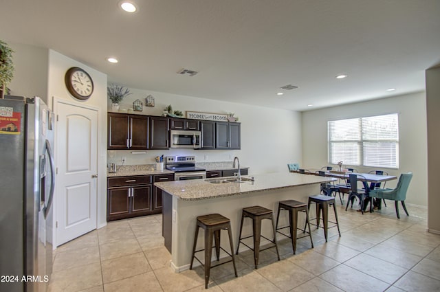 kitchen with a kitchen island with sink, a kitchen breakfast bar, sink, light stone countertops, and appliances with stainless steel finishes