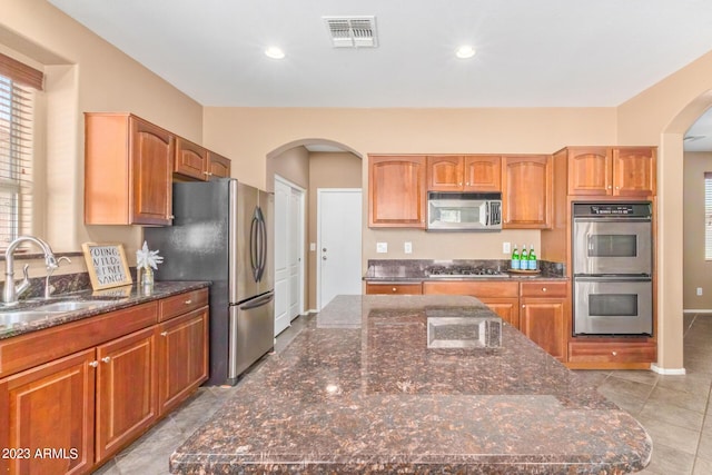 kitchen with visible vents, a sink, dark stone countertops, stainless steel appliances, and arched walkways