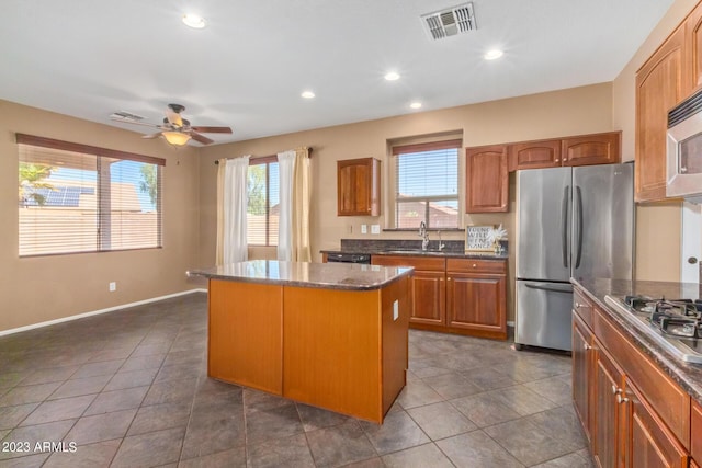 kitchen featuring visible vents, a center island, dark stone countertops, appliances with stainless steel finishes, and a sink