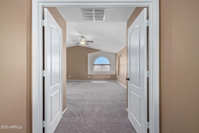 corridor with visible vents, carpet floors, baseboards, and vaulted ceiling