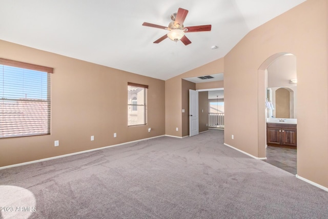 unfurnished bedroom featuring light carpet, visible vents, arched walkways, and vaulted ceiling