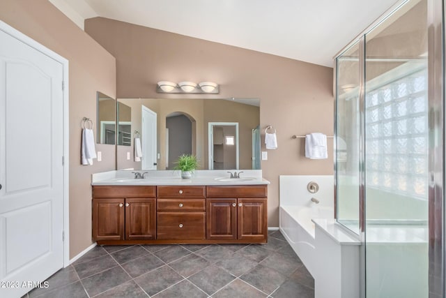 bathroom with double vanity, vaulted ceiling, a garden tub, and a sink