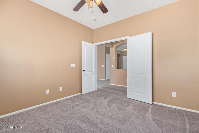 carpeted empty room with a ceiling fan, baseboards, and arched walkways