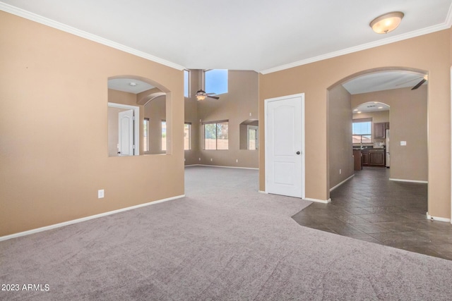 carpeted empty room with ceiling fan, arched walkways, baseboards, and ornamental molding