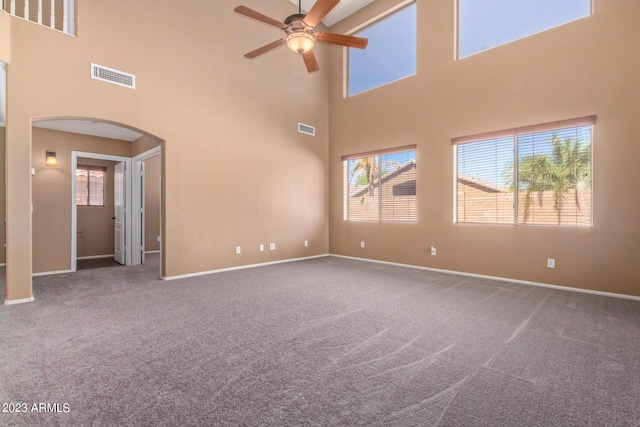 carpeted spare room featuring visible vents, arched walkways, baseboards, and a ceiling fan