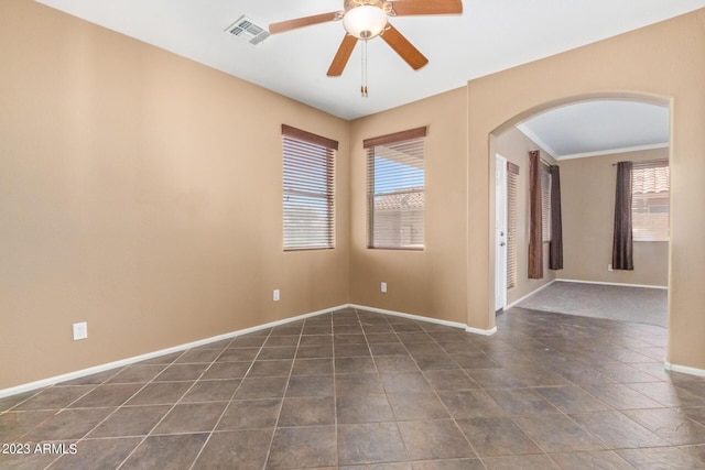 tiled empty room with visible vents, arched walkways, baseboards, and ceiling fan