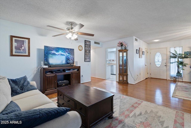 living room featuring ceiling fan, a textured ceiling, and light hardwood / wood-style floors