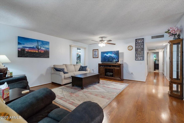 living room featuring ceiling fan, light hardwood / wood-style flooring, and a textured ceiling