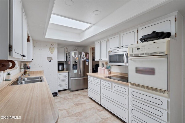 kitchen with sink, tasteful backsplash, a skylight, appliances with stainless steel finishes, and white cabinets