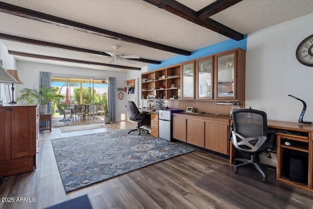 home office with dark wood-type flooring, ceiling fan, beam ceiling, built in desk, and a textured ceiling