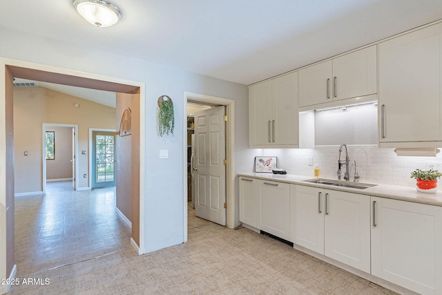 kitchen featuring lofted ceiling, sink, white cabinets, and backsplash