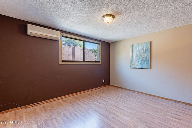 spare room with light hardwood / wood-style floors, a textured ceiling, and an AC wall unit