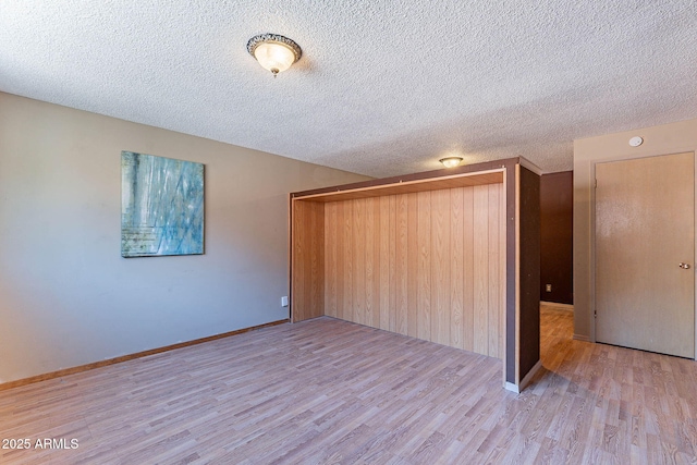 spare room with wood walls, a textured ceiling, and light hardwood / wood-style flooring