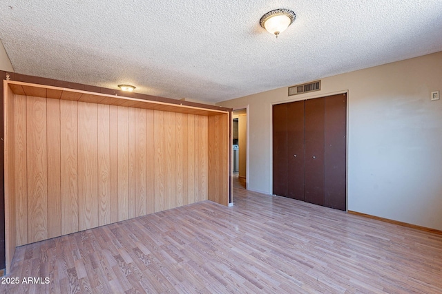 spare room featuring wooden walls, light hardwood / wood-style floors, and a textured ceiling