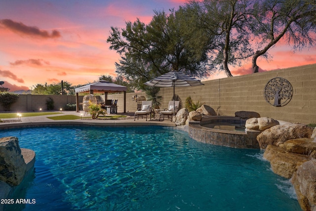 pool at dusk with a gazebo and an in ground hot tub