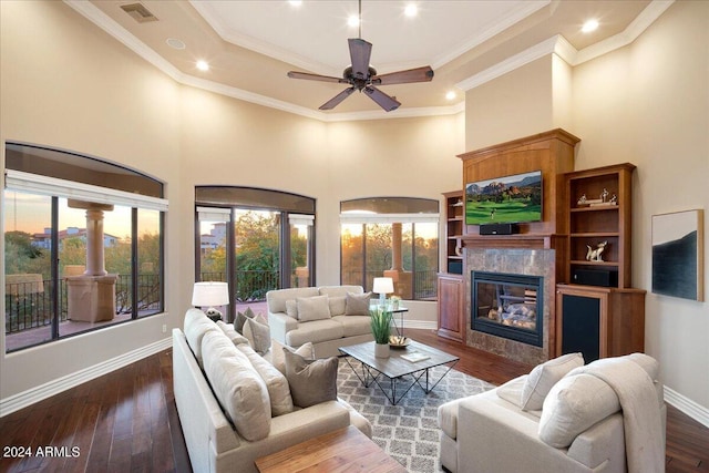 living room with ceiling fan, dark hardwood / wood-style floors, a premium fireplace, crown molding, and a towering ceiling