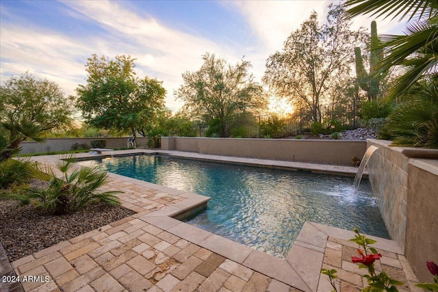 pool at dusk featuring a diving board, a patio area, and pool water feature