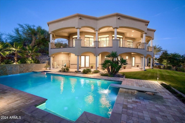 back house at dusk featuring a balcony, a patio area, and pool water feature