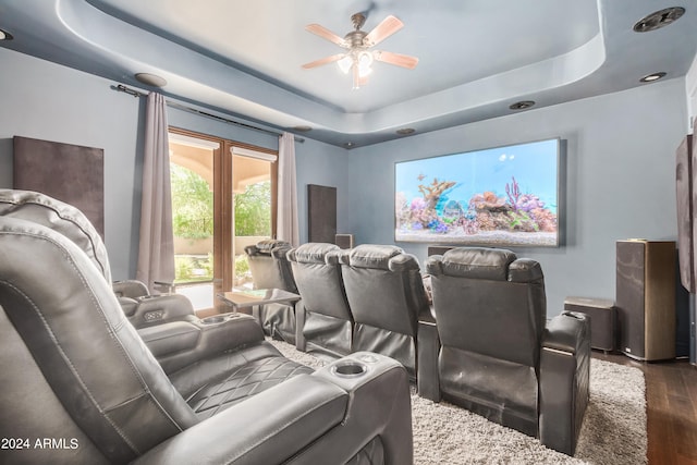 home theater room with ceiling fan, a tray ceiling, and dark hardwood / wood-style flooring