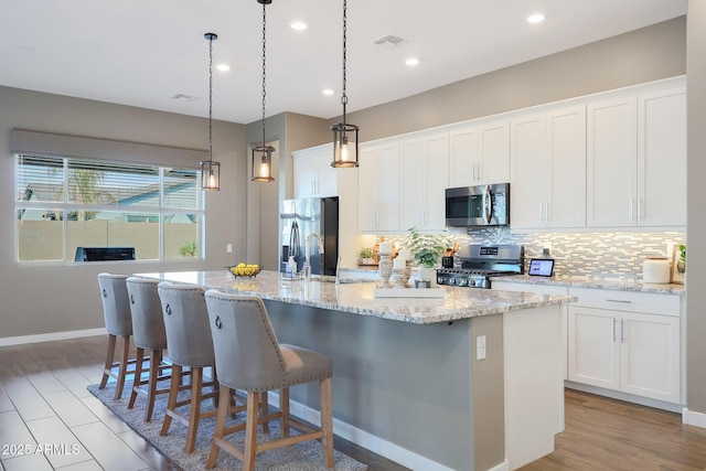 kitchen with stainless steel appliances, a center island with sink, and white cabinets