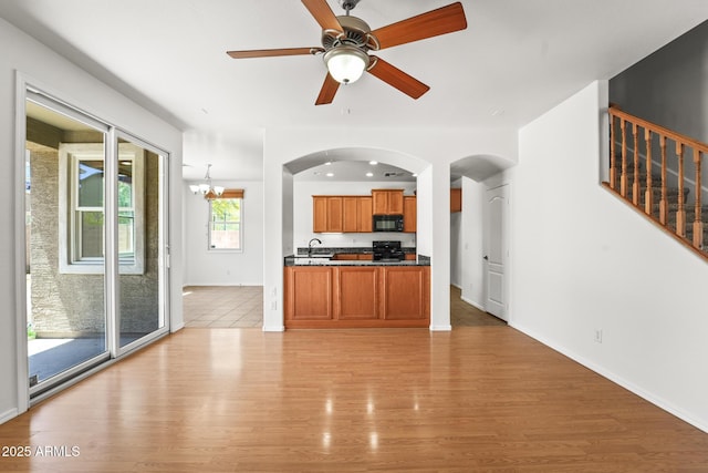 2337 E Fraktur Rd, Phoenix, AZ 85040 - unfurnished living room with arched walkways, light wood-style flooring, ceiling fan with notable chandelier, baseboards, and stairway