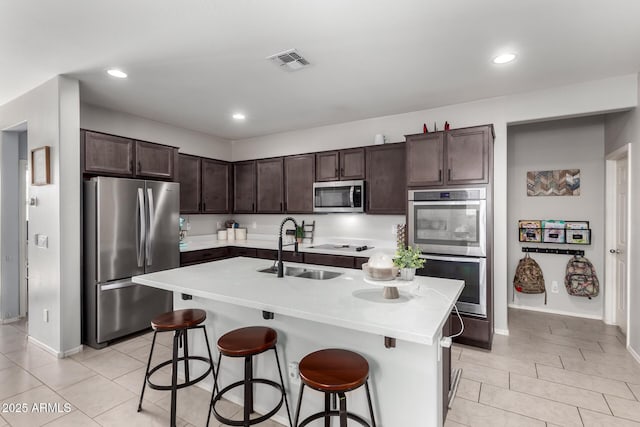 kitchen with dark brown cabinetry, visible vents, a breakfast bar area, appliances with stainless steel finishes, and a sink