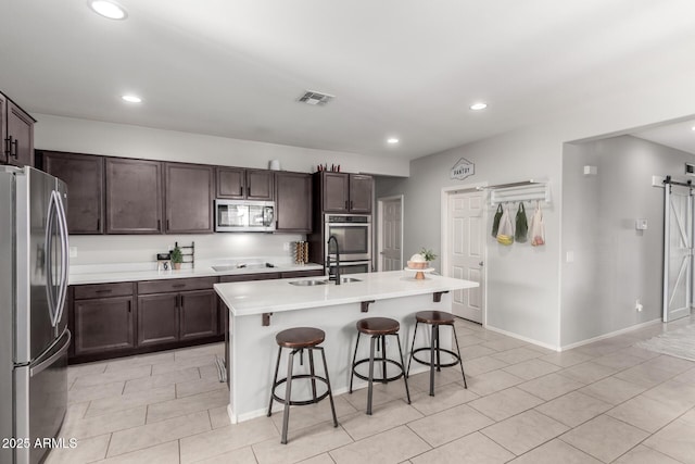 kitchen with a barn door, stainless steel appliances, a breakfast bar, a sink, and visible vents