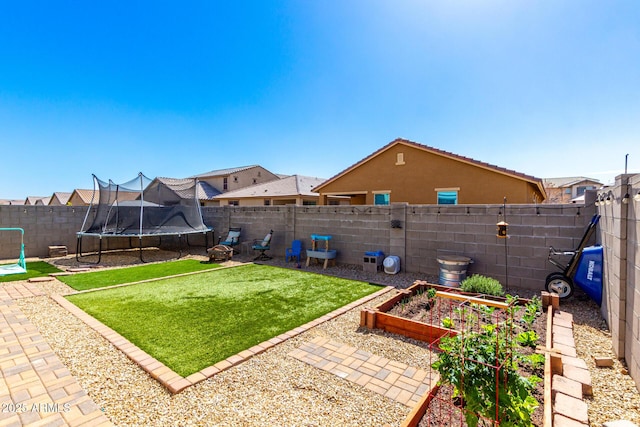 view of yard with a trampoline, a vegetable garden, and a fenced backyard