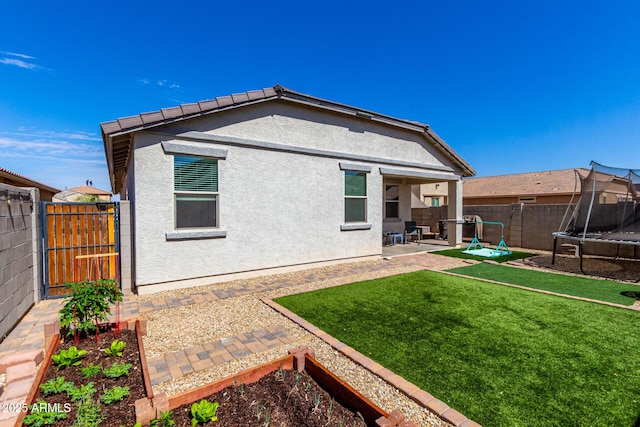 rear view of property featuring a garden, a trampoline, fence, and stucco siding