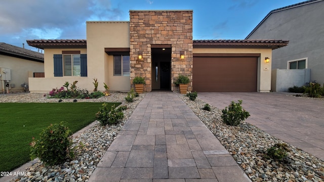 mediterranean / spanish-style house featuring decorative driveway, a tile roof, stucco siding, a front yard, and a garage