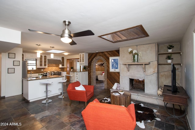 living room featuring sink, a fireplace, wooden walls, a skylight, and ceiling fan