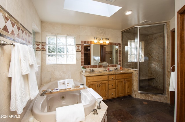 bathroom with independent shower and bath, vanity, tile walls, and a skylight