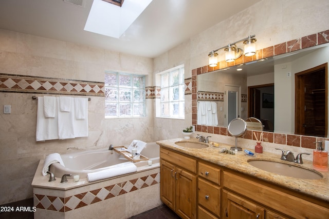 bathroom featuring tiled tub, a skylight, vanity, and tile walls