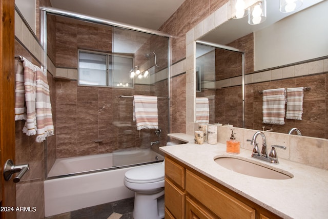 full bathroom with tile walls, shower / bath combination with glass door, vanity, and toilet