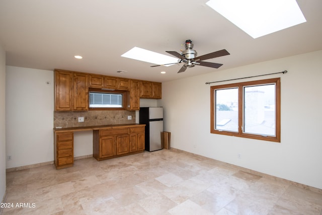 kitchen featuring stainless steel refrigerator, backsplash, ceiling fan, and a skylight