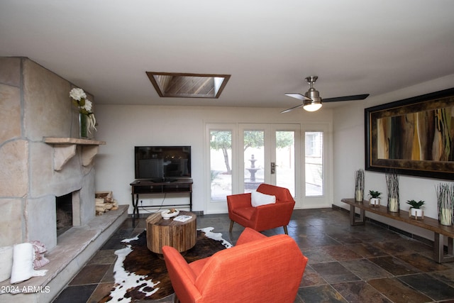 living room featuring a skylight, ceiling fan, a fireplace, and french doors