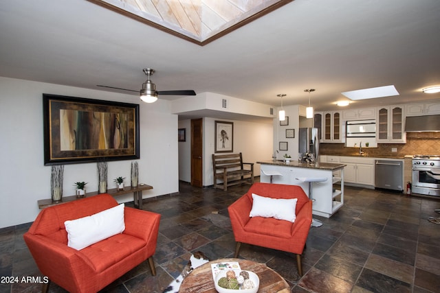 living room with ceiling fan, a skylight, and sink