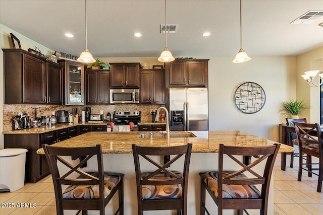 kitchen featuring an island with sink, stainless steel appliances, and decorative light fixtures