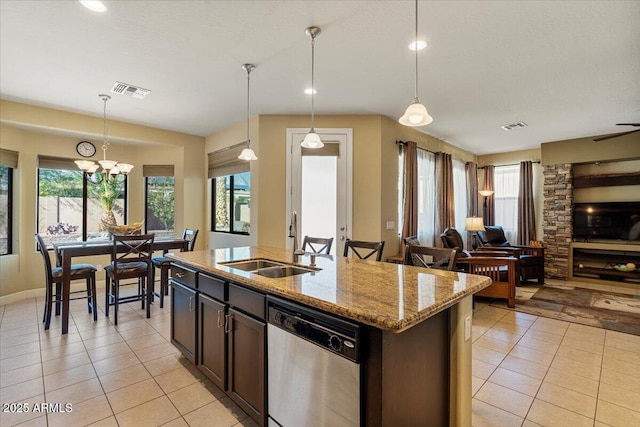kitchen featuring dishwasher, an island with sink, light stone counters, open floor plan, and hanging light fixtures