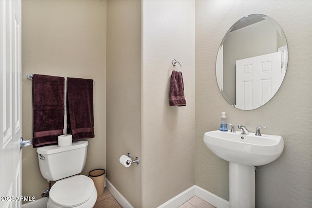bathroom with toilet, tile patterned flooring, baseboards, and a sink