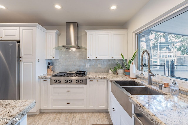 kitchen featuring appliances with stainless steel finishes, white cabinets, light wood-style flooring, and wall chimney exhaust hood