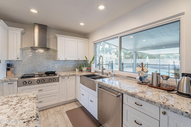 kitchen featuring wall chimney exhaust hood, a sink, white cabinets, and stainless steel appliances